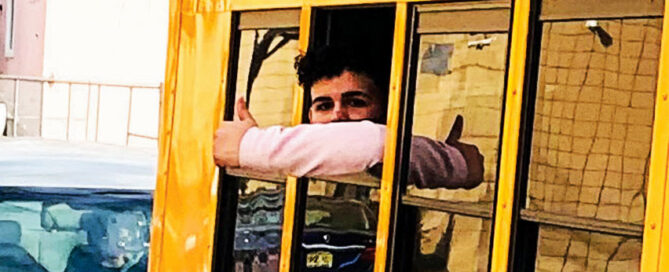 Student giving thumbs up from school bus window on arrival at school