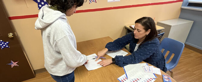 Student casting a ballot in the school's mock election with a teacher acting as a poll volunteer