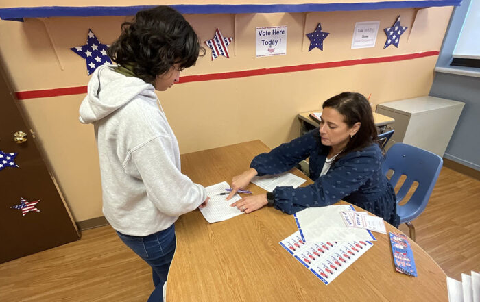 Student casting a ballot in the school's mock election with a teacher acting as a poll volunteer