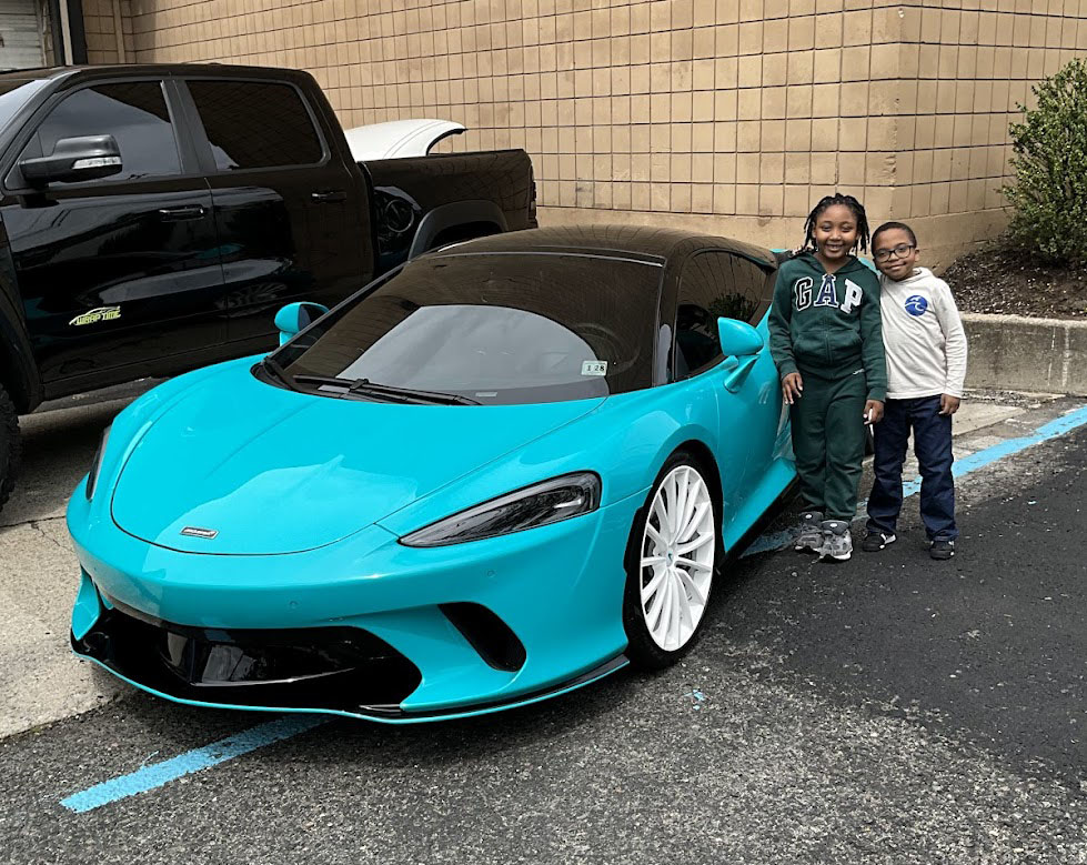 2 younger Westbridge students standing next to a turquoise super-car smiling